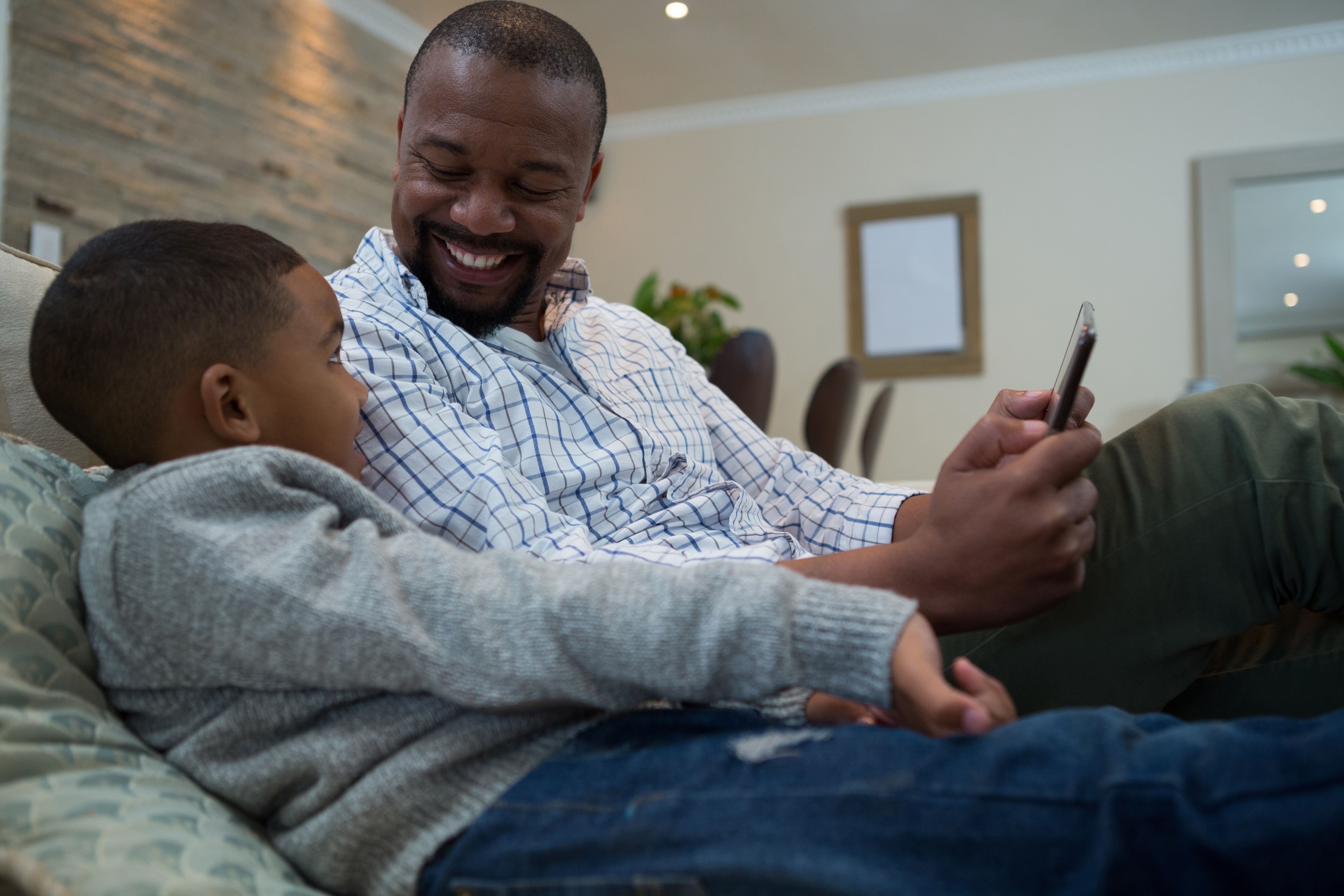 Pai e filho sentados no sofá usando o celular
