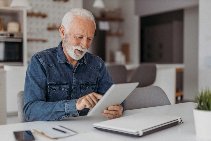 idoso sentado à mesa segurando tablet