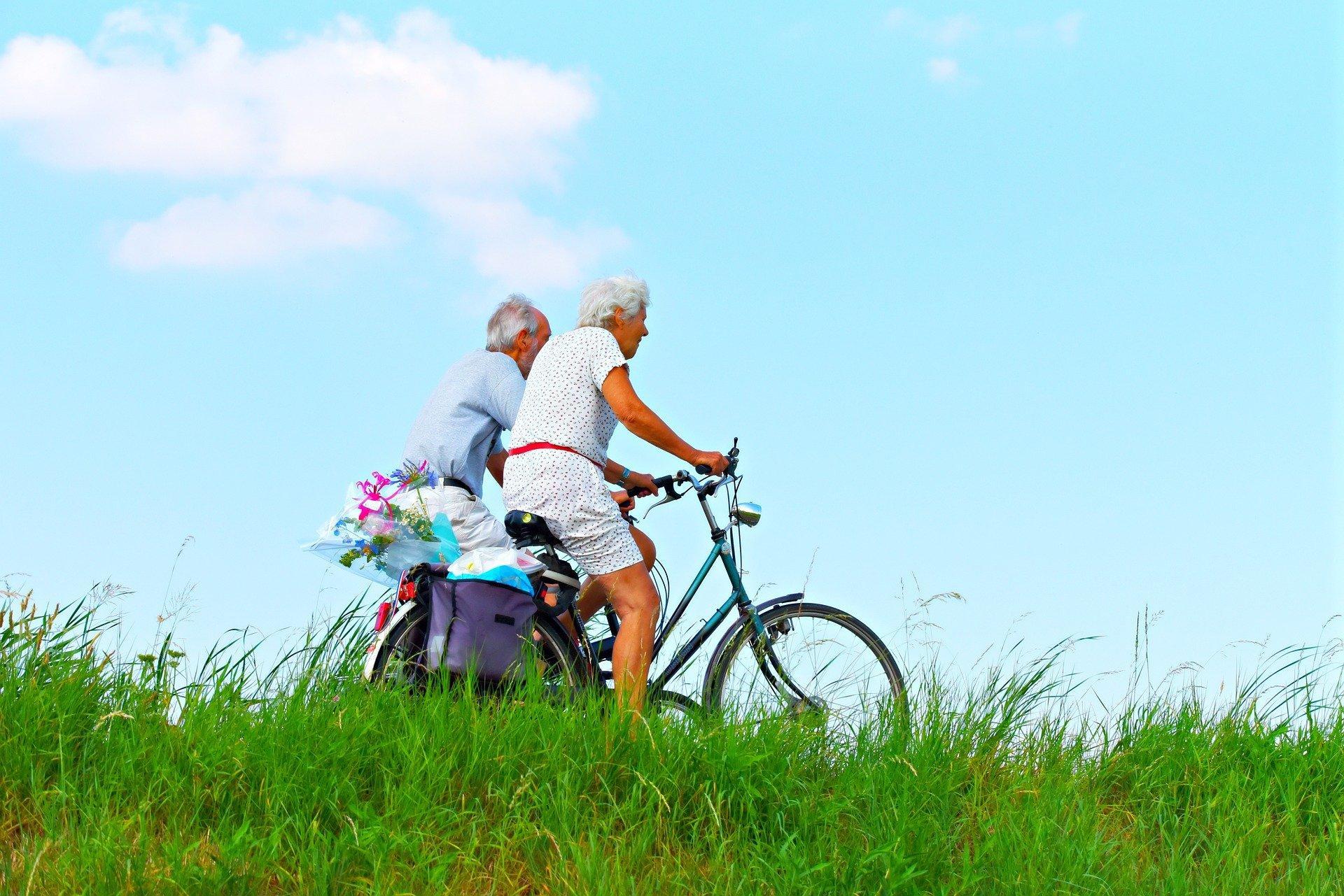 Casal de idosos se exercitando com uma bicicleta.