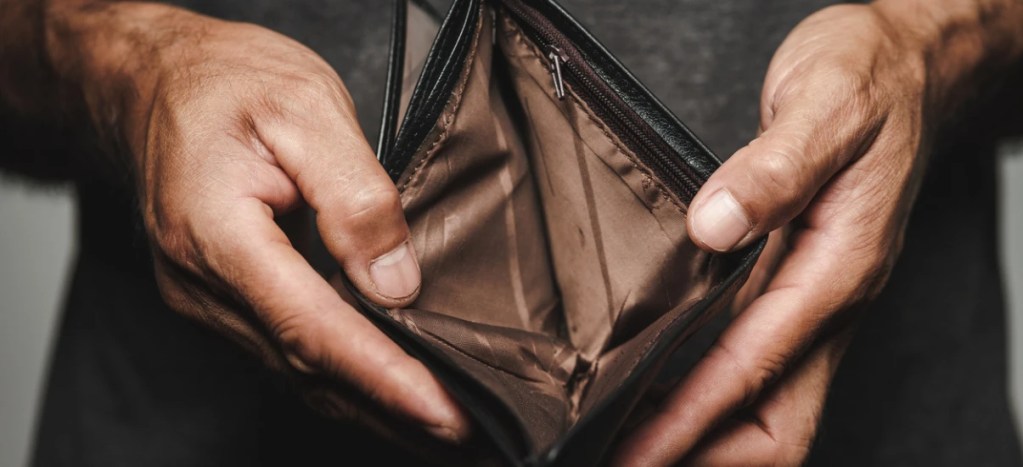 Mãos segurando uma carteira vazia, foco no interior da carteira feita de couro. Imagem ilustrativa para perda de dinheiro ou economia.