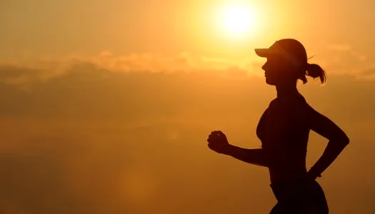 Imagem de uma mulher correndo ao pôr do sol, capturando a essência do exercício físico ao ar livre e estilo de vida saudável.