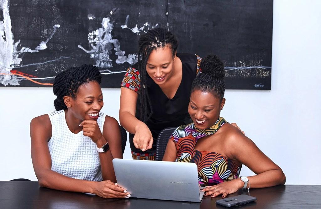 Três mulheres sentadas, analisando investimentos no computador.