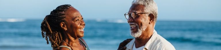 Casal de idosos se divertindo na praia, sorrindo e aproveitando o momento juntos, representando amor e felicidade na terceira idade.