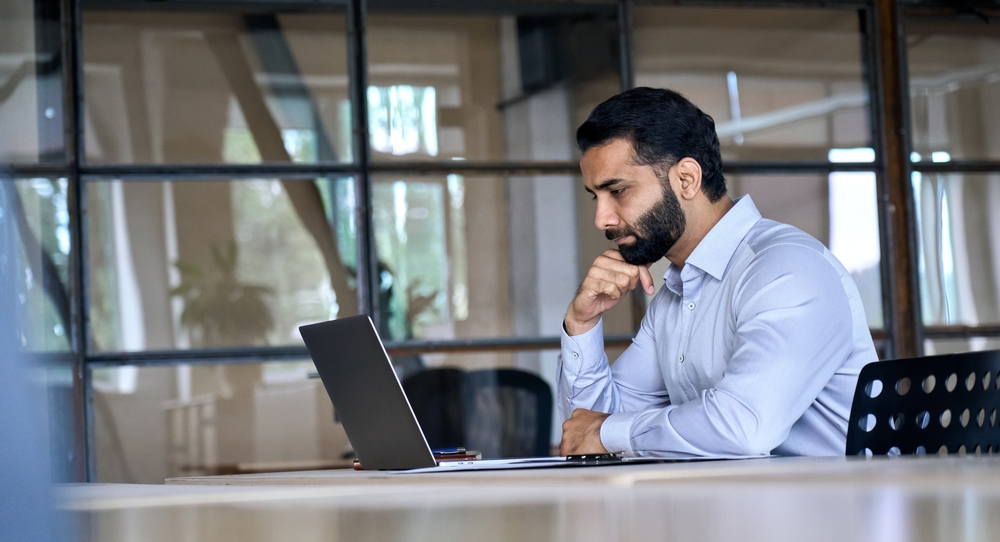 homem com camisa social sentado olhando o computador no escritório