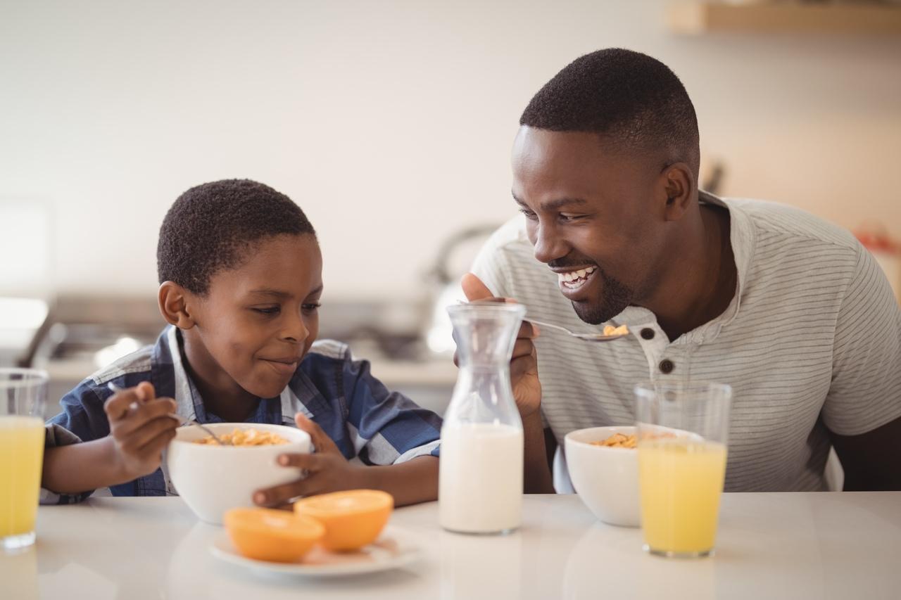 Pai e filho tomando café da manhã enquanto sorriem