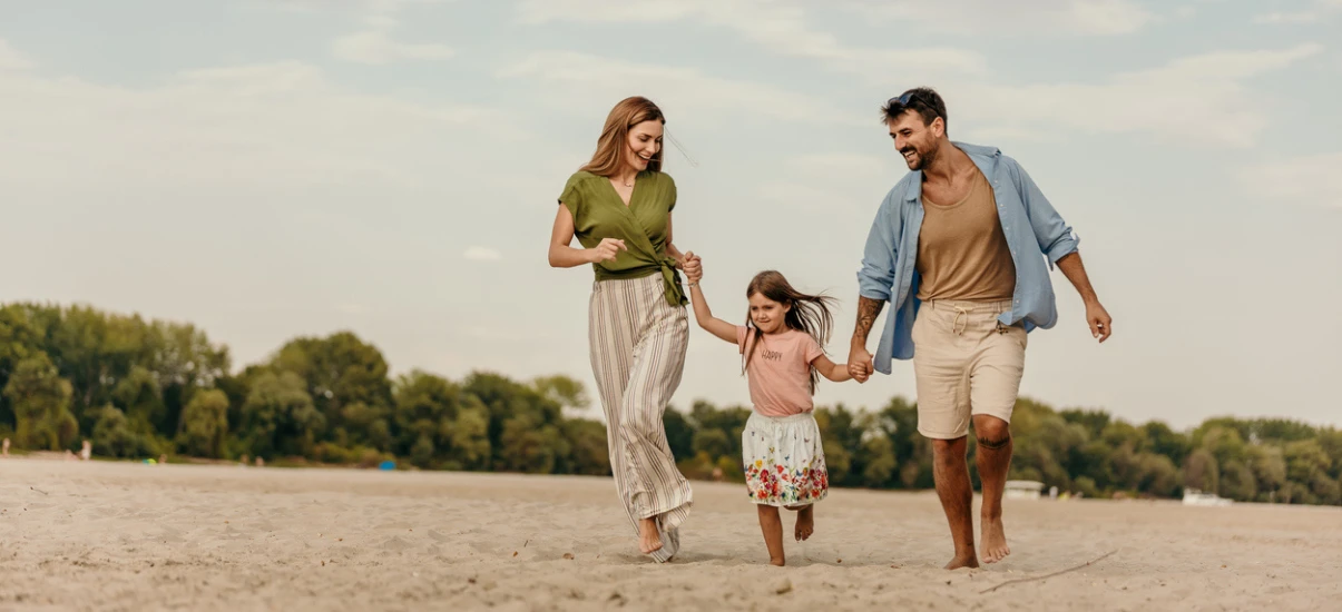Família feliz curtindo dia de praia ao ar livre, com crianças brincando na areia e céu ensolarado ao fundo.