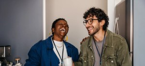 Duas pessoas felizes rindo e conversando na cozinha, celebrando uma amizade com sorriso e alegria, ambiente moderno e descontraído.