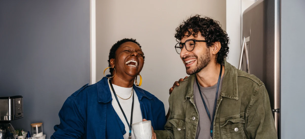 Duas pessoas felizes rindo e conversando na cozinha, celebrando uma amizade com sorriso e alegria, ambiente moderno e descontraído.