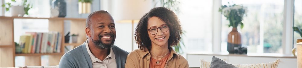 Um casal sorridente sentado em um sofá, discutindo documentos, em um ambiente aconchegante e iluminado, transmitindo felicidade e alegria.
