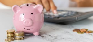 Porquinho de cerâmica rosa com moedas e de cobre ao redor, representando economia e finanças pessoais.