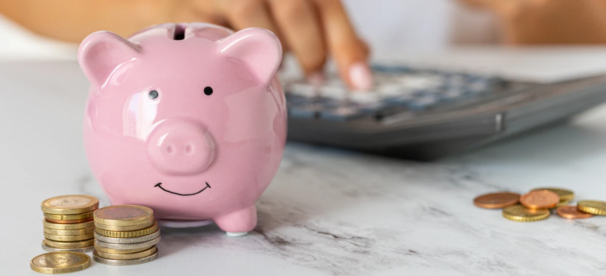 Porquinho de cerâmica rosa com moedas e de cobre ao redor, representando economia e finanças pessoais.