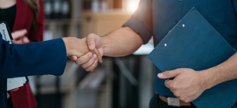 Imagem de um aperto de mão entre duas pessoas em um ambiente profissional, símbolo de acordo ou parceria de negócios.