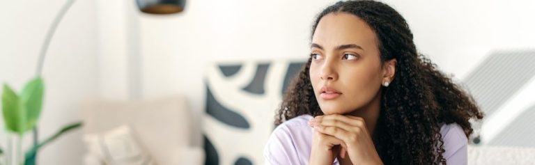 Mulher pensativa sentada no sofá em um ambiente moderno, refletindo sobre a vida enquanto observa a decoração ao redor.
