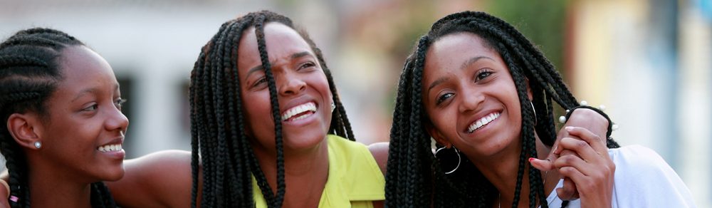 Três mulheres sorrindo e se divertindo em um ambiente externo, expressando amizade e felicidade.