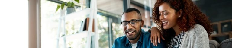 Um casal sorridente revisando documentos em uma mesa de café, com anotações e xícaras ao redor, em um ambiente acolhedor e iluminado.