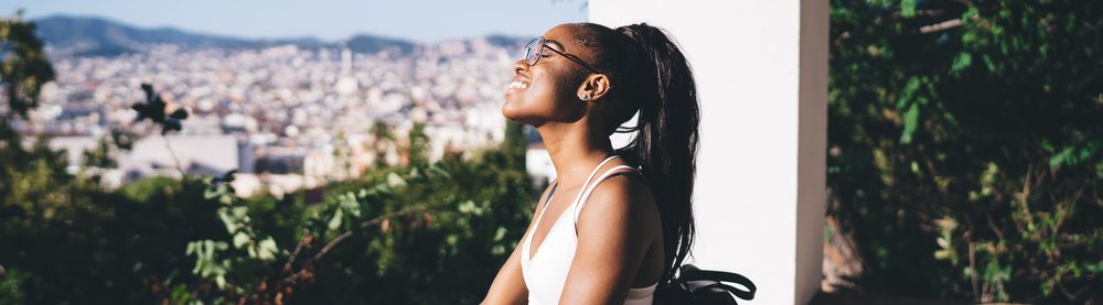 Mulher sorridente sentada em uma varanda, desfrutando da vista da cidade em um dia ensolarado.