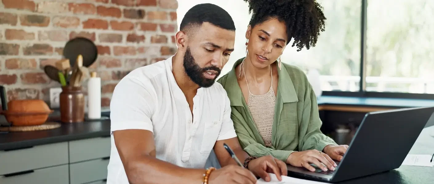 casal em frente a bancada com computador e papeis, lidando com contas e documentos
