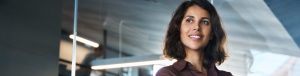Profissional feminina com camisa marrom, sorrindo e demonstrando confiança em ambiente de escritório moderno.