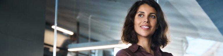 Profissional feminina com camisa marrom, sorrindo e demonstrando confiança em ambiente de escritório moderno.