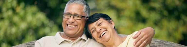 Casal sorridente sentado em um banco de parque, simbolizando amor e felicidade na terceira idade, aproveitando momentos juntos ao ar livre.