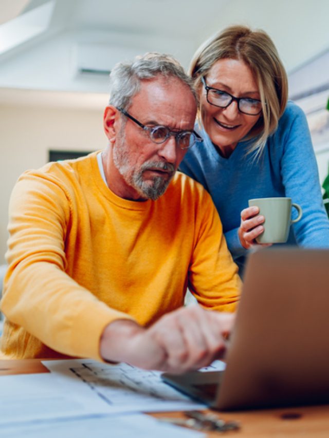 Senior middle aged happy couple using laptop together at home