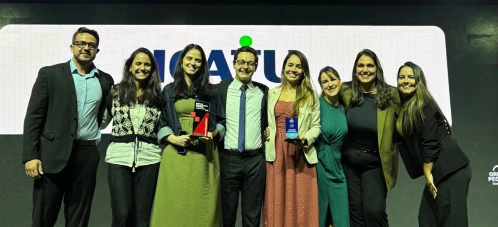 Grupo de pessoas comemorando vitória na premiação da GPTW, com troféus nas mãos e sorrindo para a câmera