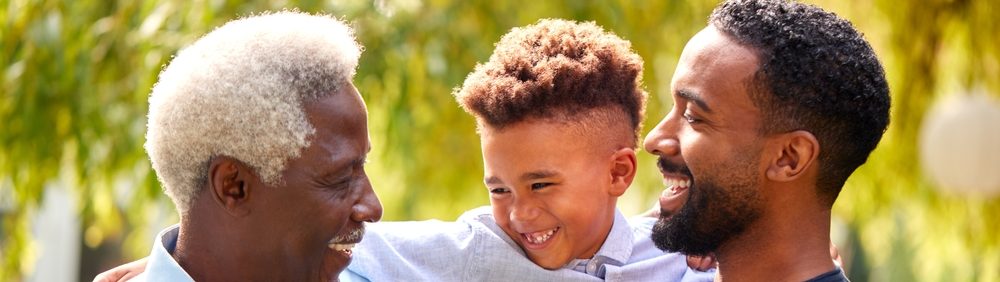 Uma família feliz composta por um avô, pai e filho, sorrindo juntos em um ambiente ao ar livre.