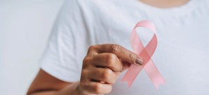 Pessoa segurando um laço rosa, símbolo de conscientização contra o câncer de mama, em um fundo branco, em uma campanha de prevenção e saúde.