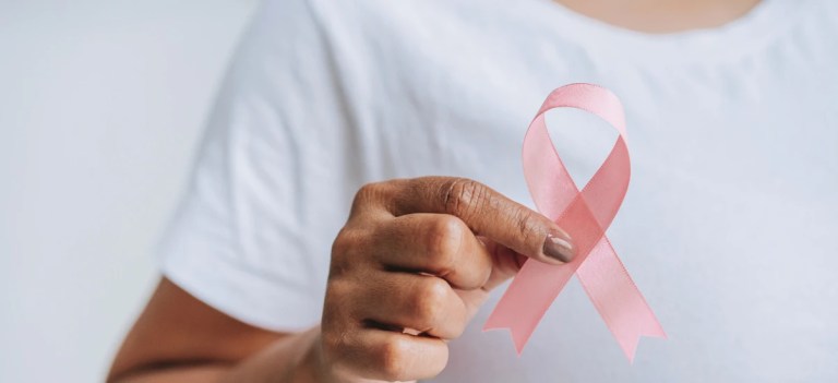 Pessoa segurando um laço rosa, símbolo de conscientização contra o câncer de mama, em um fundo branco, em uma campanha de prevenção e saúde.