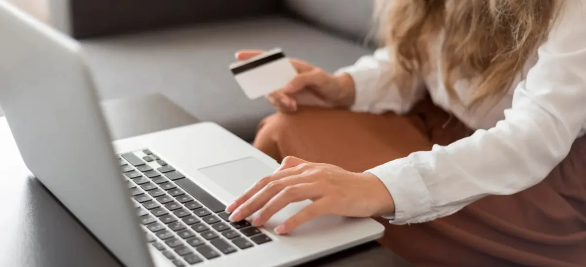 Mulher usando laptop e cartão de crédito, realizando compras online, em ambiente doméstico confortável, foco em comércio eletrônico e compras pela internet.