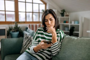 mulher sentada no sofá olhando o celular com afeição apreensiva
