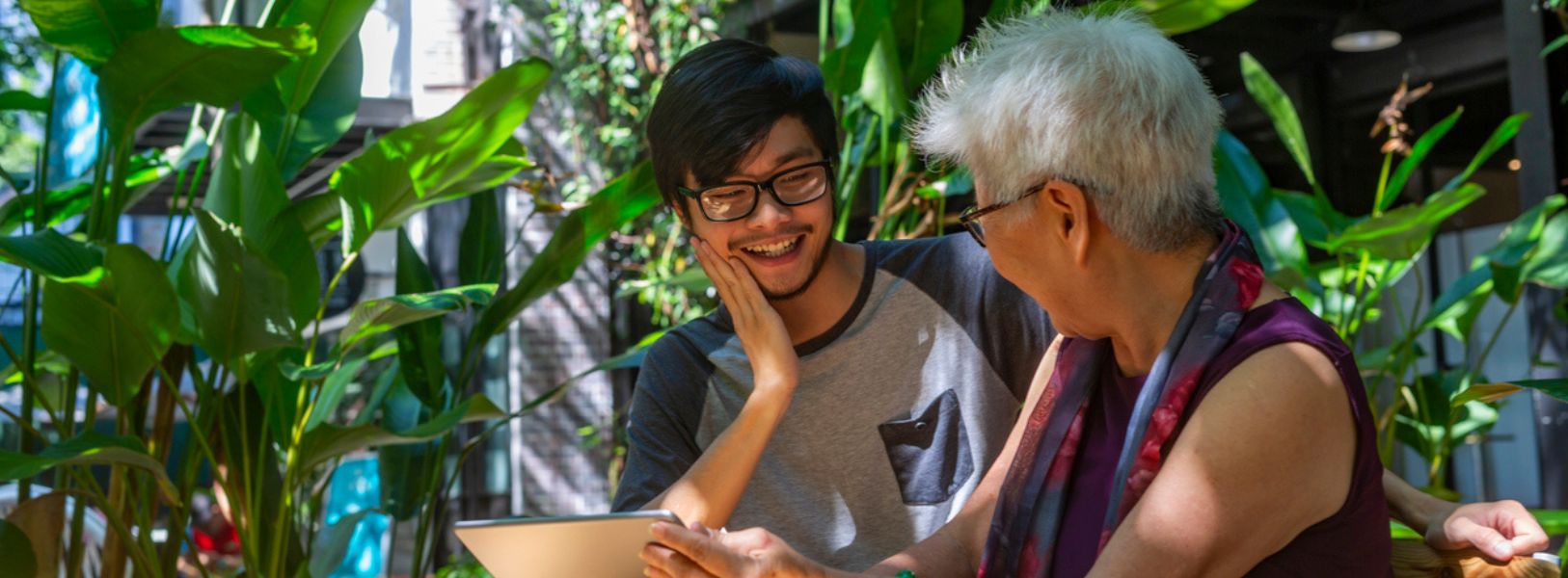 mulher idosa segurando um tablet, olhando sorrindo para jovem ao seu lado, também sorrindo