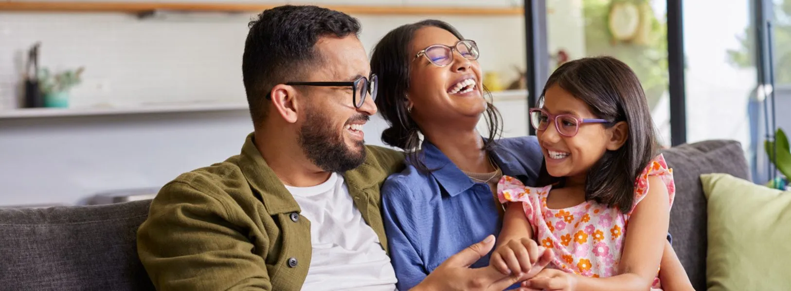 casal sorrindo se abraçando junto à filha no sofá