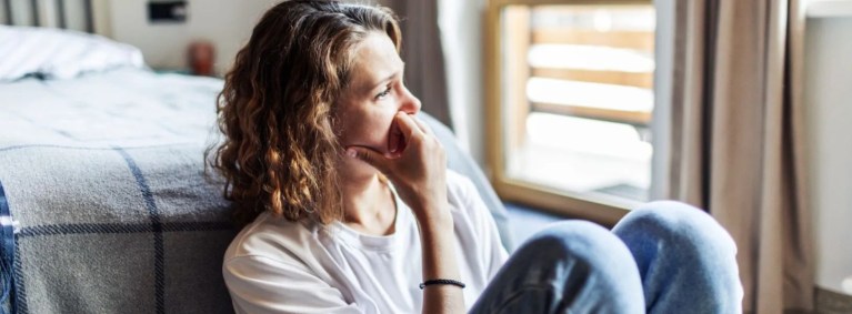 mulher sentada sozinha ao lado da cama no quarto com o rosto triste e olhar pensativo