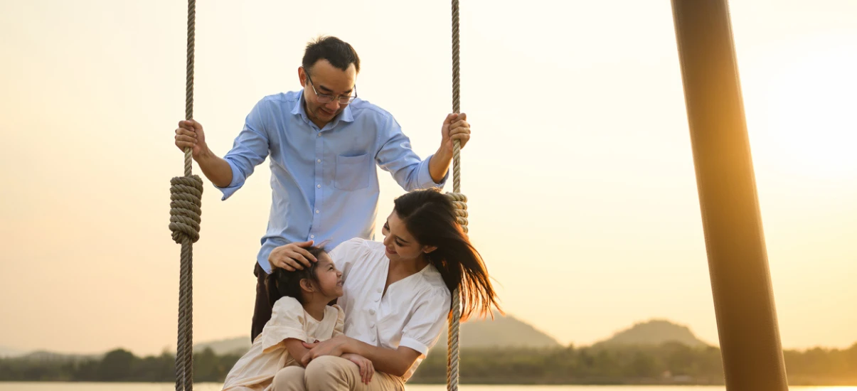 Família feliz em um balanço ao pôr do sol, promovendo momentos de união e alegria ao ar livre.
