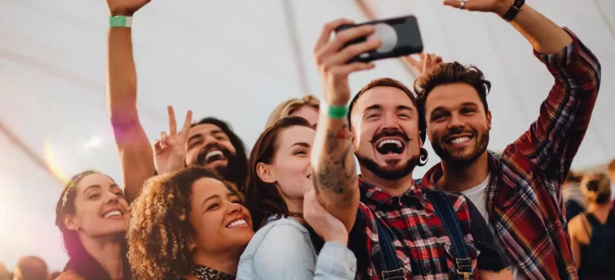 Grupo diversificado de amigos sorrindo e tirando uma selfie em um evento ao ar livre, transmitindo alegria e conexão, ideal para momentos festivos.