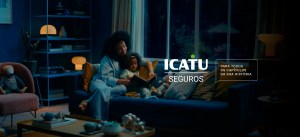 Imagem retratando mãe e filha sentadas confortavelmente no sofá, lendo juntas. A cena transmite uma sensação de acolhimento e segurança, destacando a mensagem da ICATU Seguros.