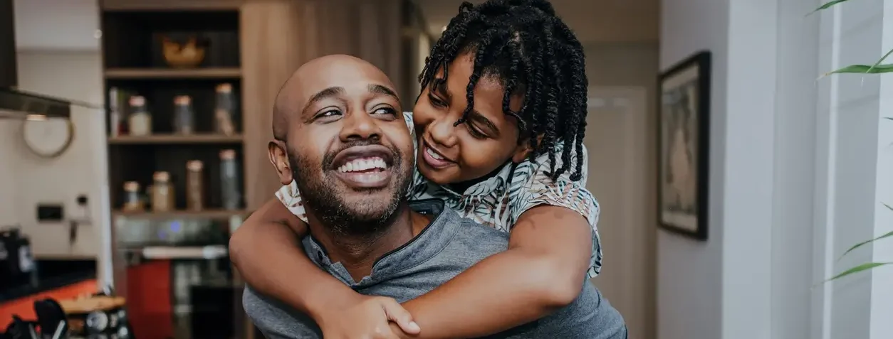 Homem sorridente carrega seu filho nas costas dentro de casa ambos estão felizes brincando