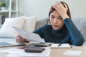 Mulher preocupada analisando documentos financeiros em casa, expressando estresse com contas ou dívidas.
