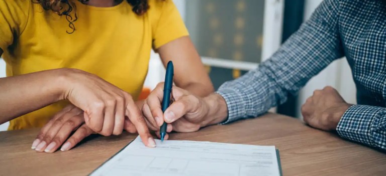 Duas pessoas assinando documento em ambiente de escritório, símbolo de contratos e negociações comerciais.