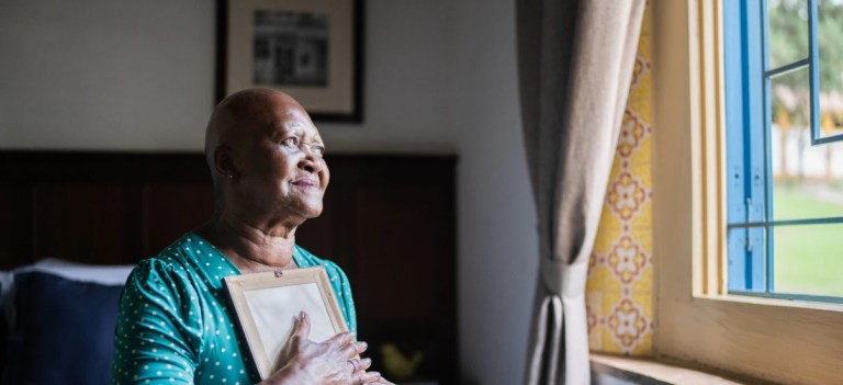 Idosa contemplando a vista da janela em um ambiente interno.