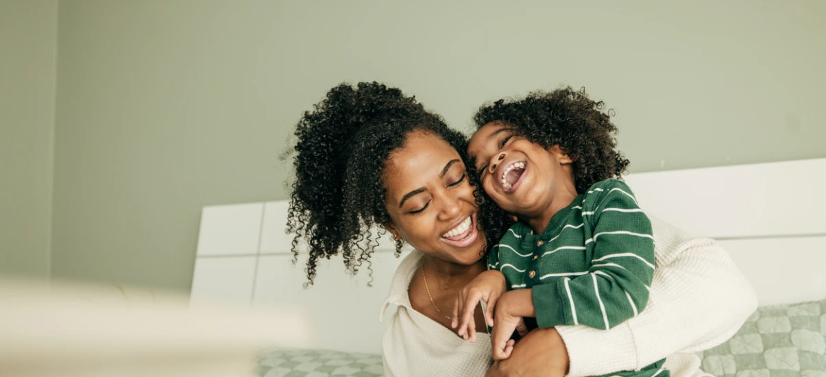 Mãe e criança sorrindo juntas, demonstrando amor e alegria em um momento de ligação familiar.