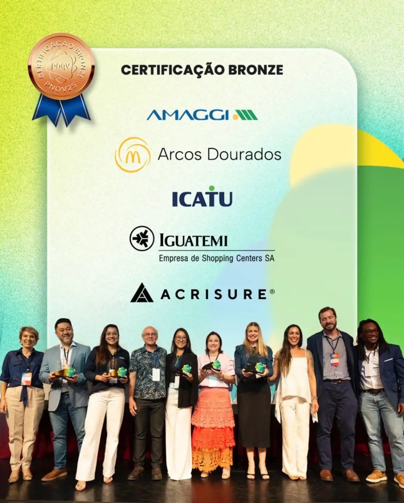 Grupo de pessoas celebrando conquista de certificação bronze, com destaque para as logomarcas de empresas e uma medalha de reconhecimento ao fundo.