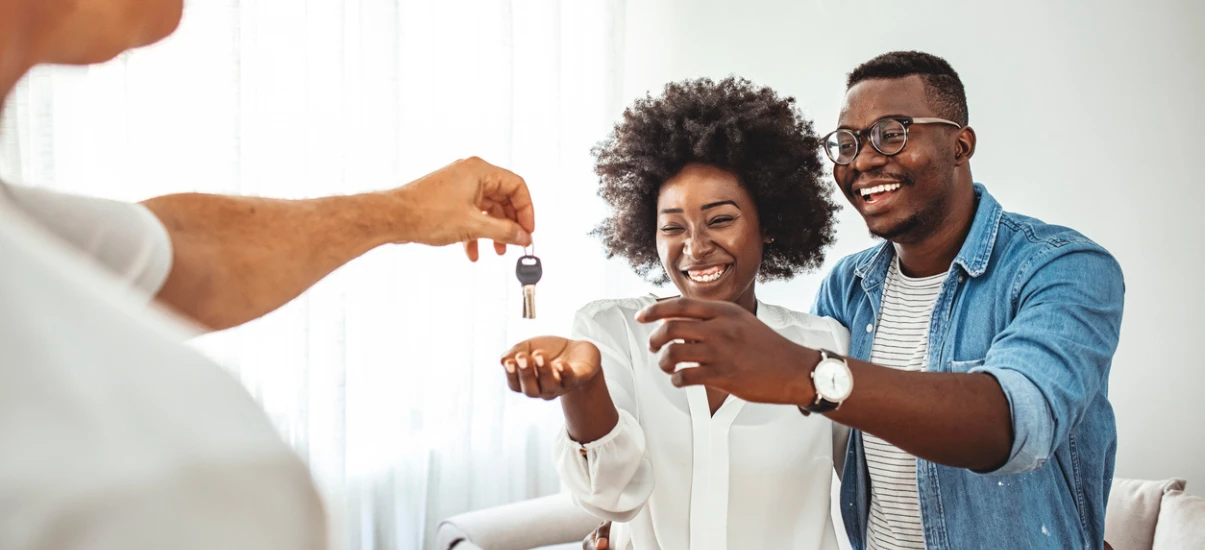 Casal feliz recebendo as chaves de um imóvel novo de um vendedor, símbolo de conquista e realização de um sonho imobiliário.