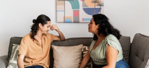 Duas pessoas em uma conversa emocional sentados em um sofá na sala, uma delas aparentando estar chateada ou triste.