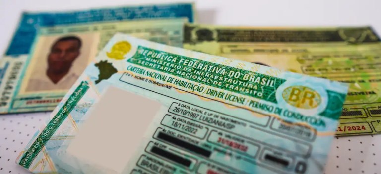 Documentos e carteiras de motorista do Brasil, focados em habilitação e registro de veículos, sobre uma mesa com fundo branco. Itens usados para documentos oficiais.