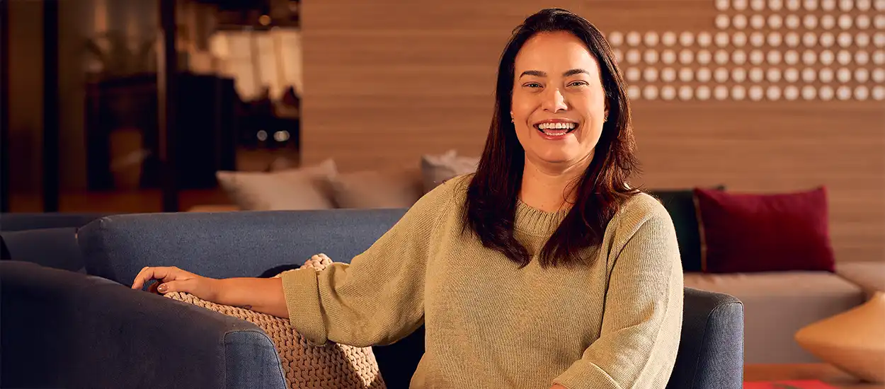 Mulher sorridente sentada em sofá confortável na sala de estar moderna e acolhedora, transmitindo felicidade e bem-estar.