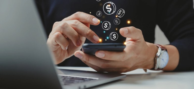 Pessoa manipulando smartphone com ícones de dólar e símbolos de dinheiro flutuando, representando finanças, investimentos ou dinheiro digital.