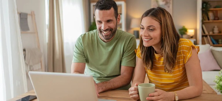 Casal olhando o computador sentado na mesa de jantar.