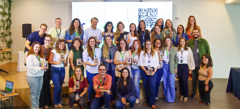 Grupo de profissionais participando de evento ou workshop com ambiente moderno, telas digitais e QR code ao fundo, promovendo networking e conhecimentos na área de tecnologia ou educação.